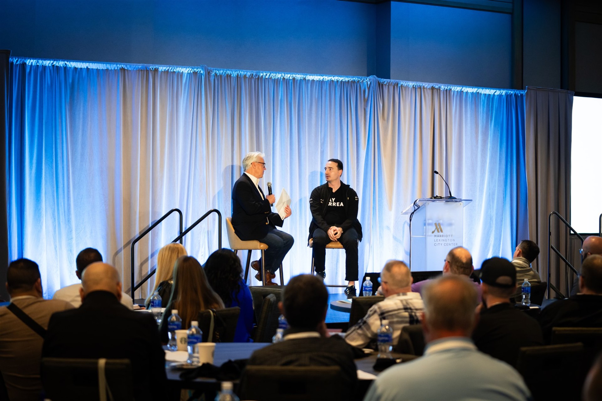 David Kain interviewing a guest on stage in front of a live audience